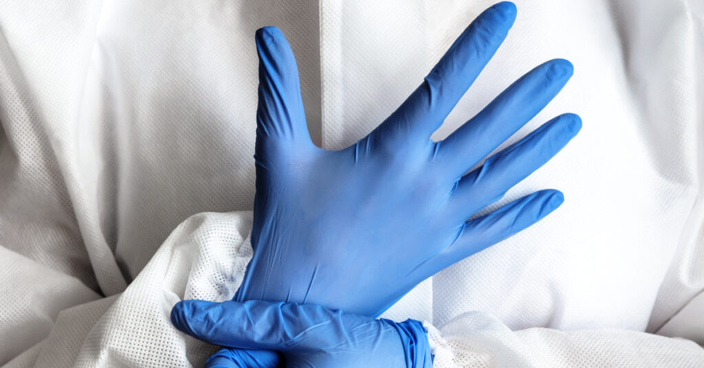 An individual is wearing a white protective suit and a pair of blue gloves. They are adjusting the fit of the gloves.