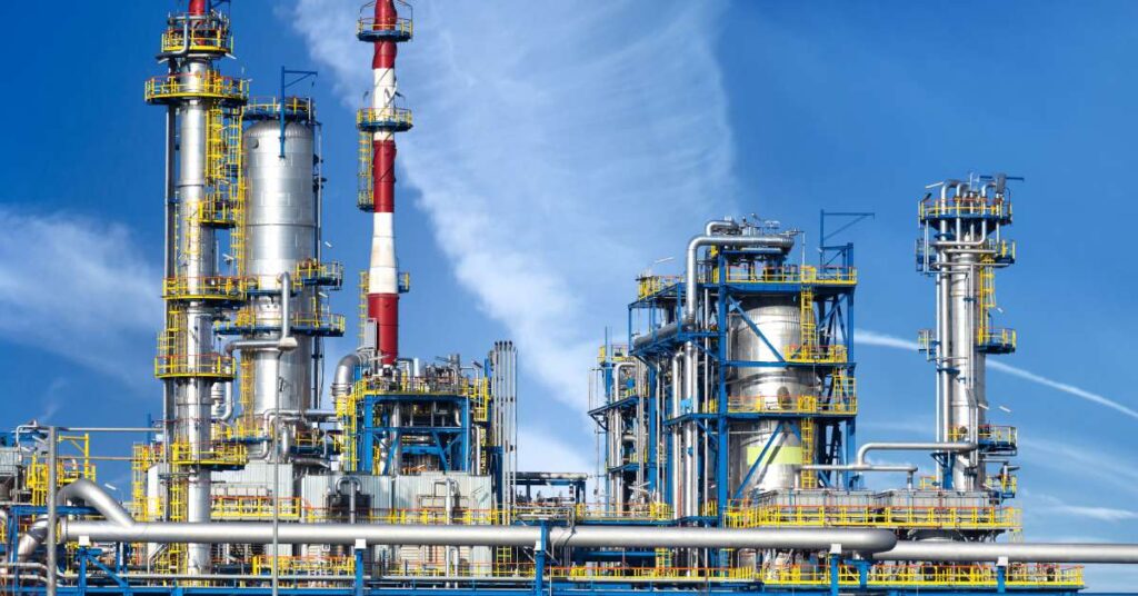 The exterior of a large oil refinery on a sunny day. There are several large tanks throughout the refinery.