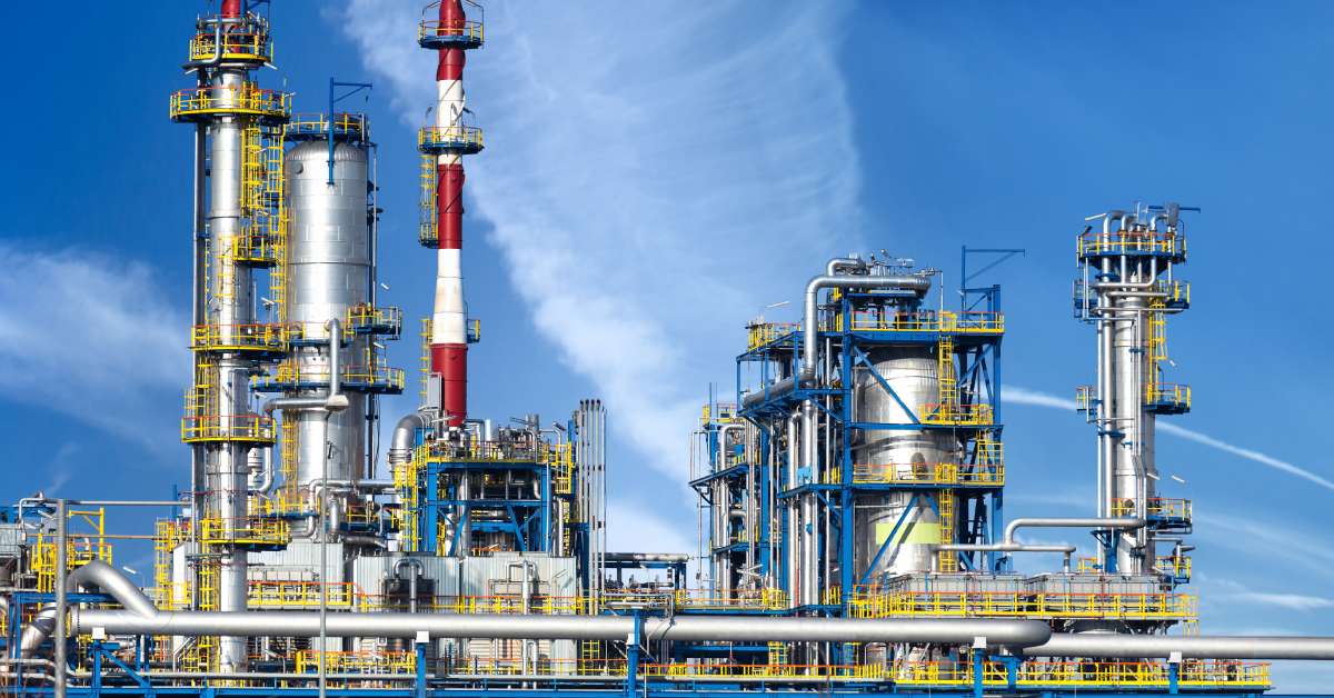 The exterior of a large oil refinery on a sunny day. There are several large tanks throughout the refinery.