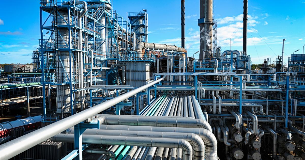 A large oil and gas refinery on a sunny day. There are metal tubes, containers, scaffolding, and funnels.