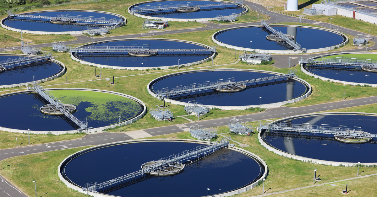 An aerial view of a wastewater treatment facility with several large circular tanks of water with scaffolding.