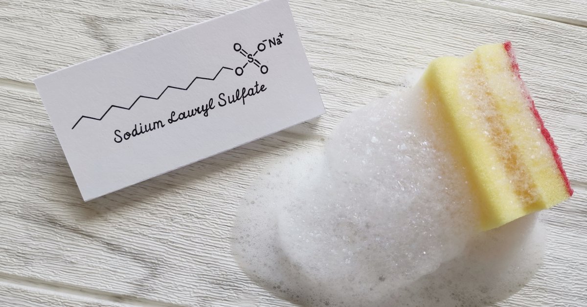The structural chemical formula of sodium lauryl sulfate drawn on a card, next to it is a sponge covered with foam.