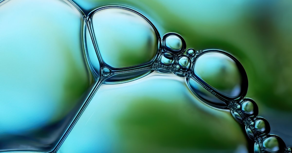 Green-colored, transparent bubbles of different sizes, including large bubbles and tiny bubbles, produced in a liquid.