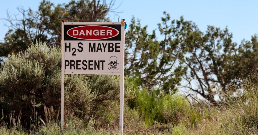 A sign that warns about the dangerous presence of hydrogen sulfide gas posted among grass and trees.