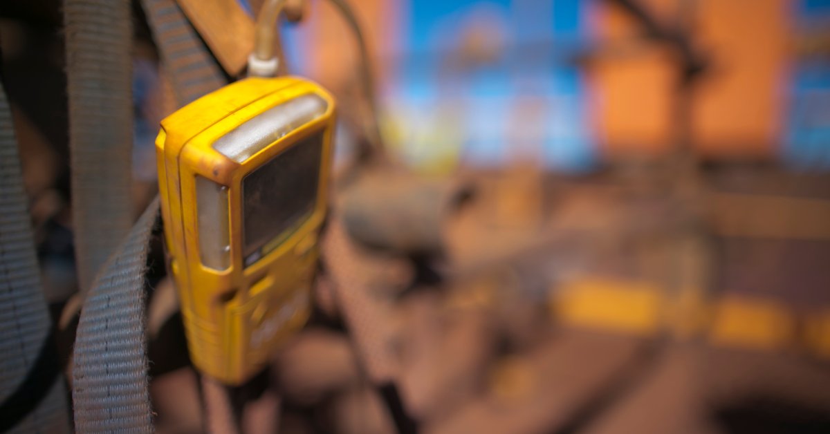 A yellow gas detection monitor affixed to a dark-colored strap at the entrance of an industrial worksite.