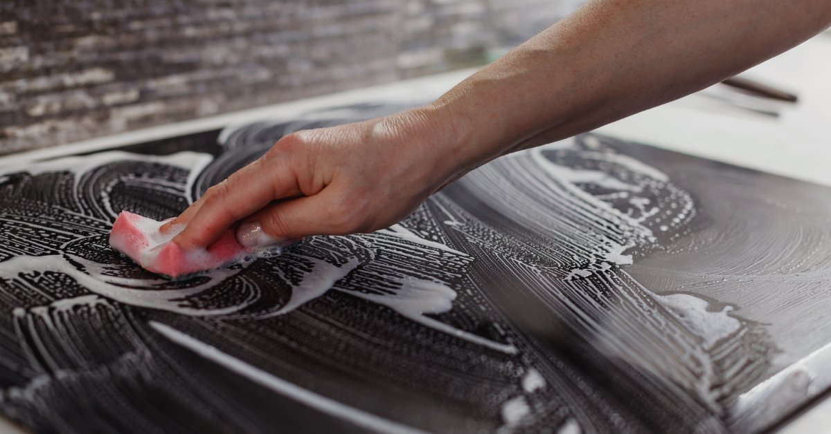 A person's right hand pressing a pink sponge to a black surface. White foam covers the sponge and the black surface.