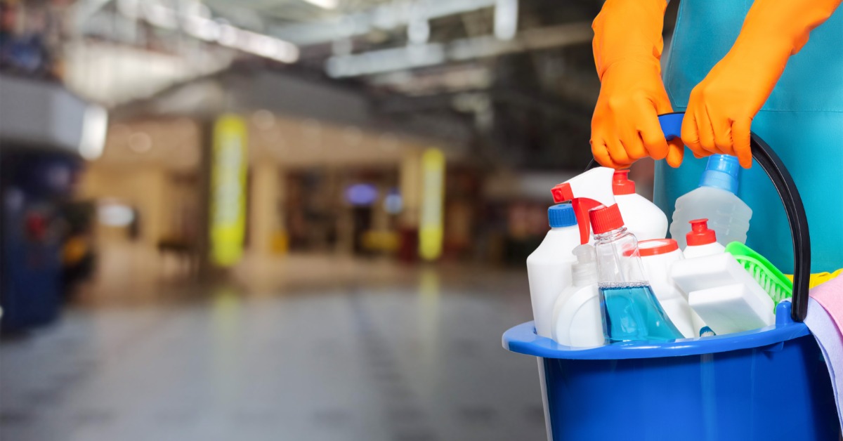 A close-up of someone wearing orange gloves and using cleaning supplies and tools in industrial premises.