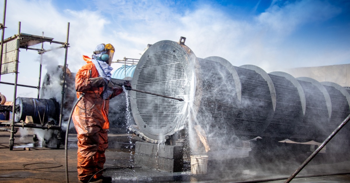 Factors Impacting the Effectiveness of Industrial Degreasers A close-up of professional power cleaning a tube bundle with a high-pressure water jet under a cloudy blue sky.