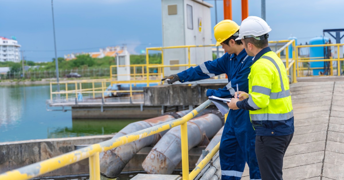Two environmental engineers work at wastewater treatment plants. They're both wearing yellow safety helmets.