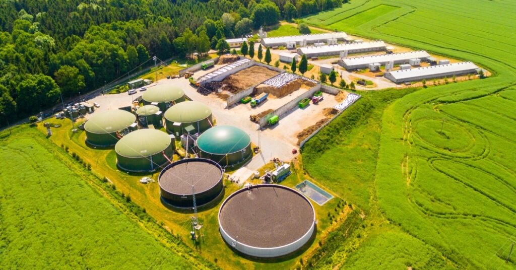 An aerial view of a biogas plant and a farm in green fields. It's a renewable energy plant made from biomass.