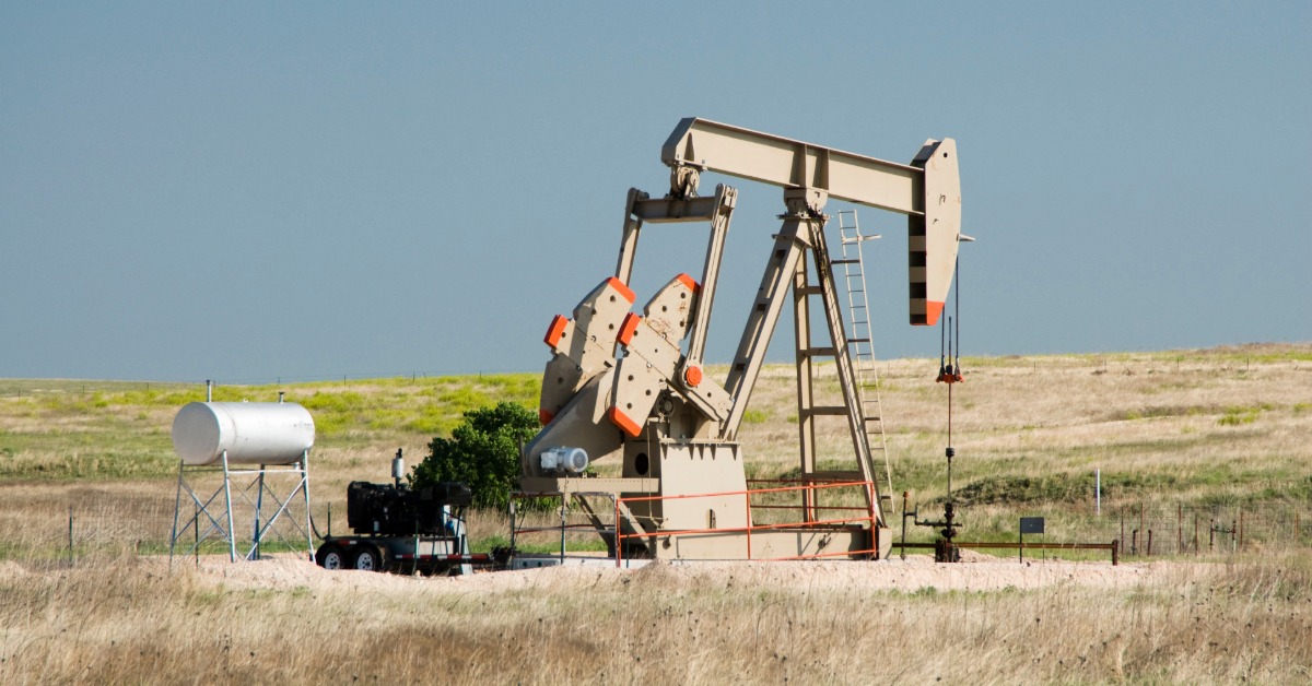 Oil pump jack operating in open grassland, with storage tank and equipment under clear sky in rural landscape