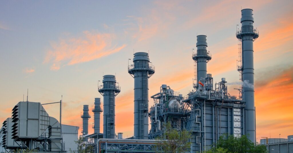 Industrial power plant with tall smokestacks and complex machinery operating at sunset in an energy production facility.