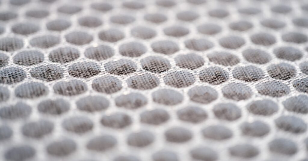 Close-up of gray honeycomb-textured material with rows of rounded cells fading into soft focus across the surface.
