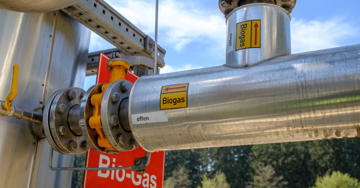 A close-up of large silver industrial pipes that are labeled 'Biogas' in yellow and red lettering and labeling.